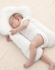 Baby sleeping on a white U-shaped pillow on a beige surface
