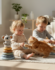 Two children playing with a cat on a rug in a bright living room.