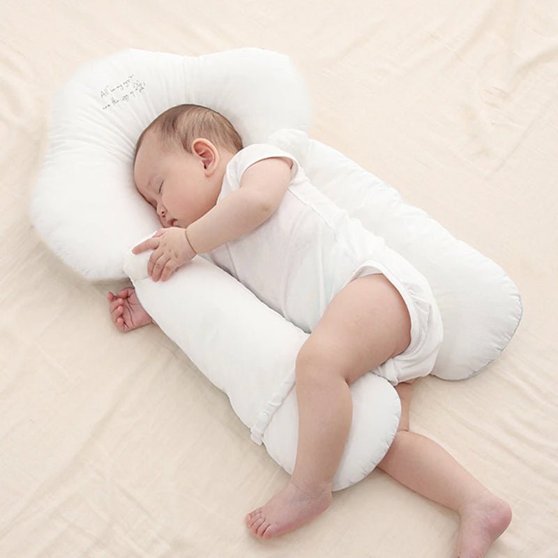 Baby sleeping on a white U-shaped pillow on a beige surface